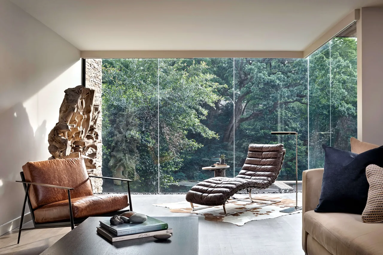 Modern living room features floor-to-ceiling glass walls with views of lush greenery outside.