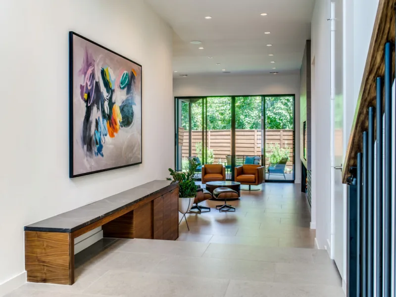 Modern interior hallway with leather swivel chairs and black-framed sliding glass doors opening to a fenced outdoor space.