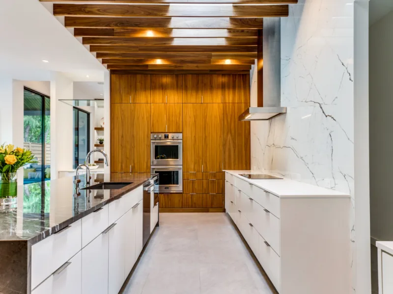 Riverview kitchen features white cabinetry, a wood-paneled wall with built-in ovens, and a dark marble island under a wood slat ceiling.
