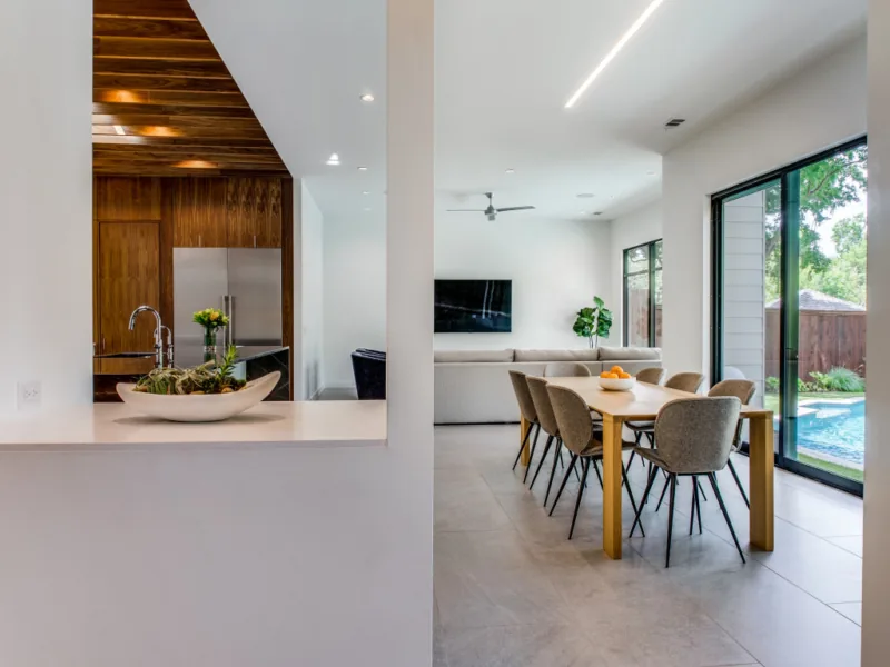 Open dining area with wooden table and upholstered chairs adjacent to living space with large sliding glass doors.