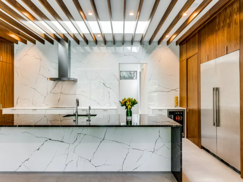 Kitchen featuring marble countertops and backsplash, wood-paneled cabinetry, and a stainless steel refrigerator with a built-in wine cooler.