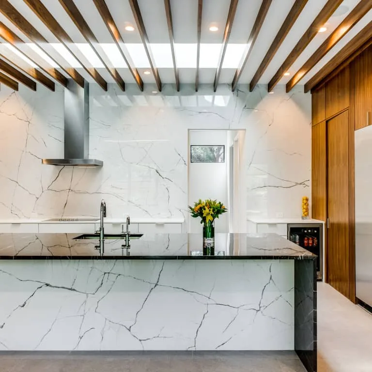 Riverview kitchen by Eckxstudio features a marble island, wood ceiling beams, and stainless steel appliances in a modern design.