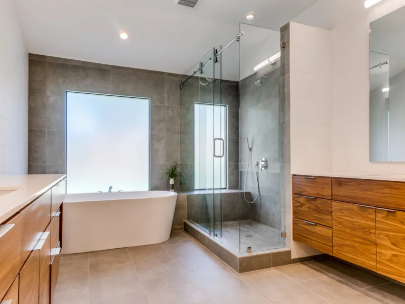 Bathroom featuring a freestanding tub under frosted window, glass shower, and wood vanity cabinets.