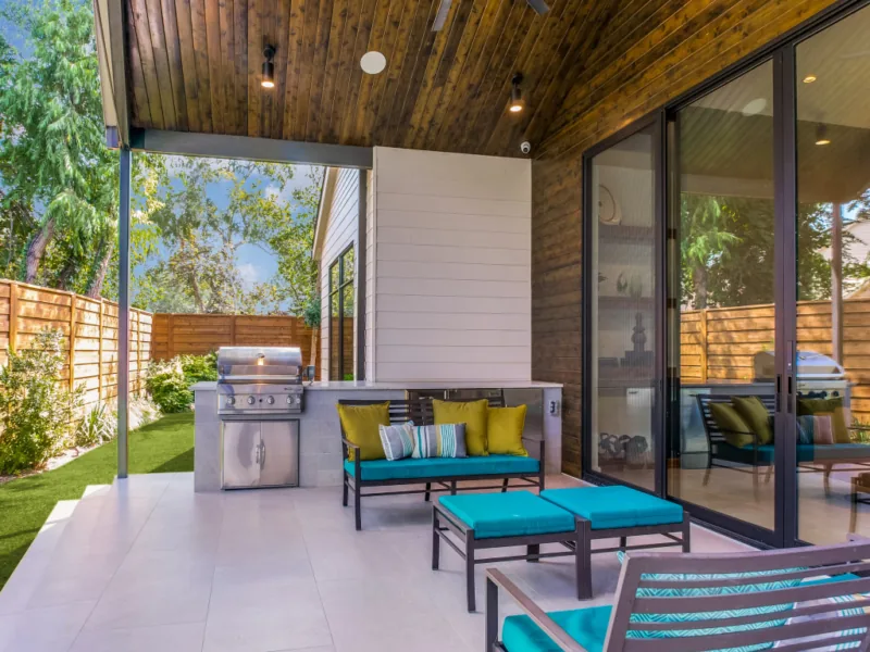 Covered patio features wood-paneled ceiling, built-in stainless grill, and turquoise cushioned seating.