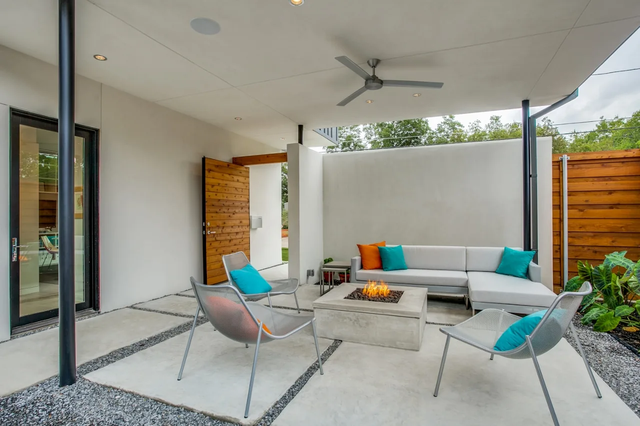 Covered outdoor living space featuring a concrete fire pit and seating with bright cushions.