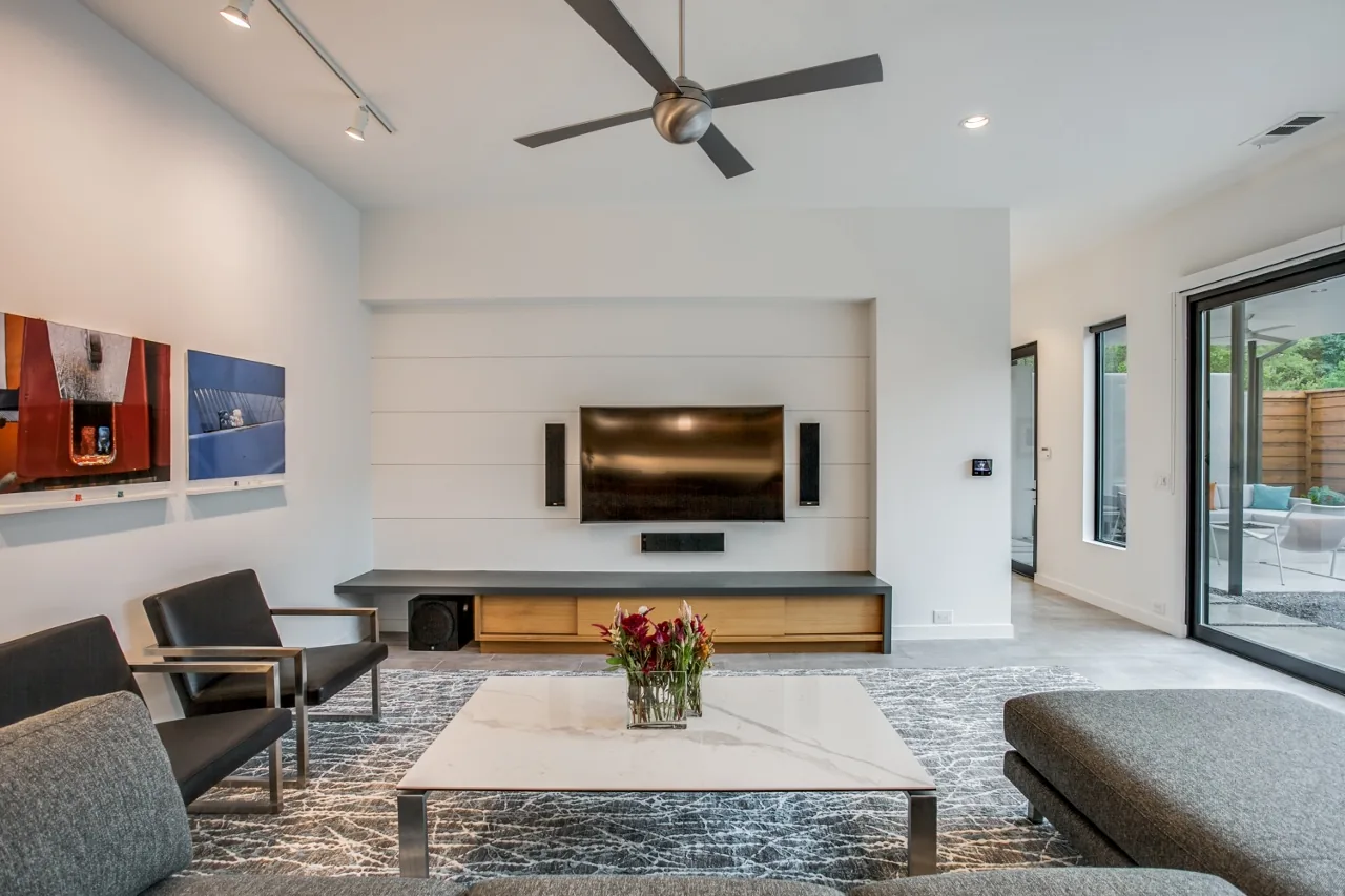Living room featuring a gray sectional sofa, patterned area rug, and a wall-mounted flat screen TV with speakers.