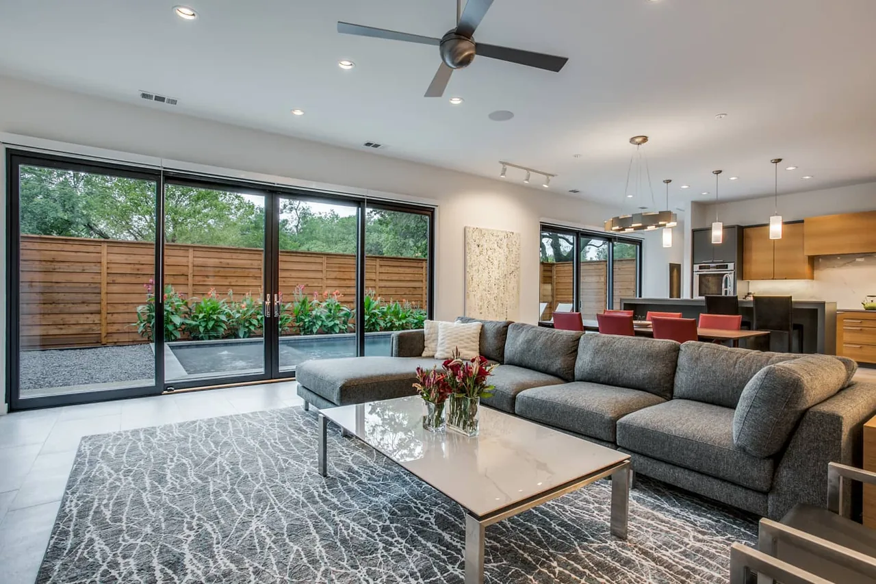 Living room with gray sectional sofa, patterned rug, and dining area with red chairs in project:Barcode by Eckxstudio.
