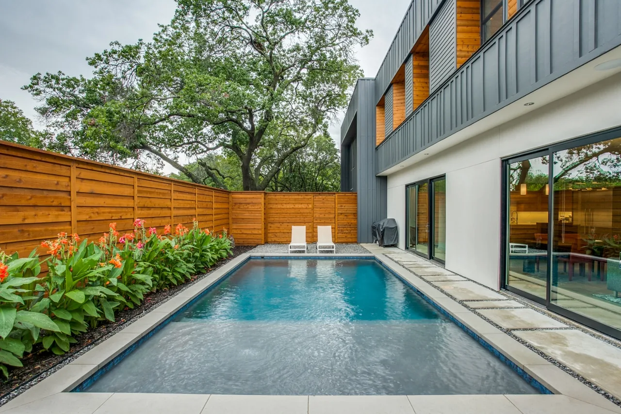 Modern backyard with a rectangular pool, wood privacy fence, and sliding glass doors of a house.