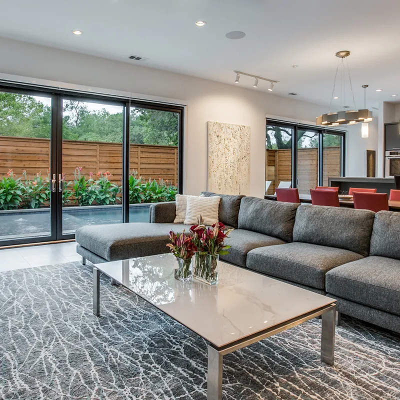 Living room with gray sectional, marble coffee table, and large sliding glass doors facing a wooden fenced yard.
