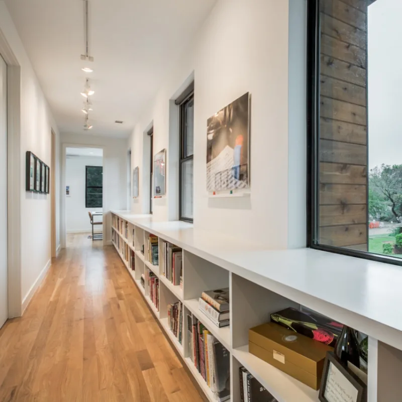 Hallway features white built-in bookshelves beneath windows and wood flooring with track lighting overhead.