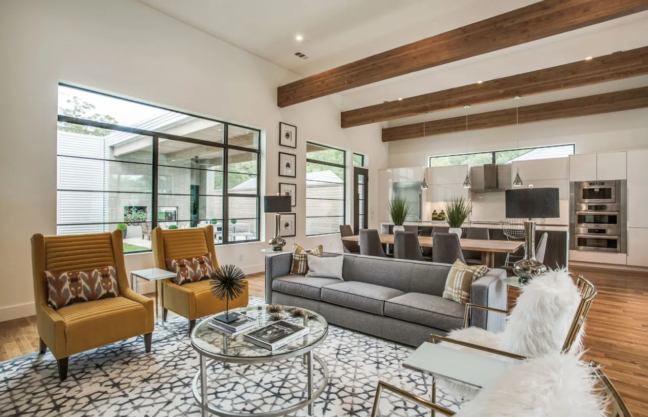 Open-plan living and dining area with exposed wood beams and large black-framed windows in the Ribbon House by Eckxstudio.