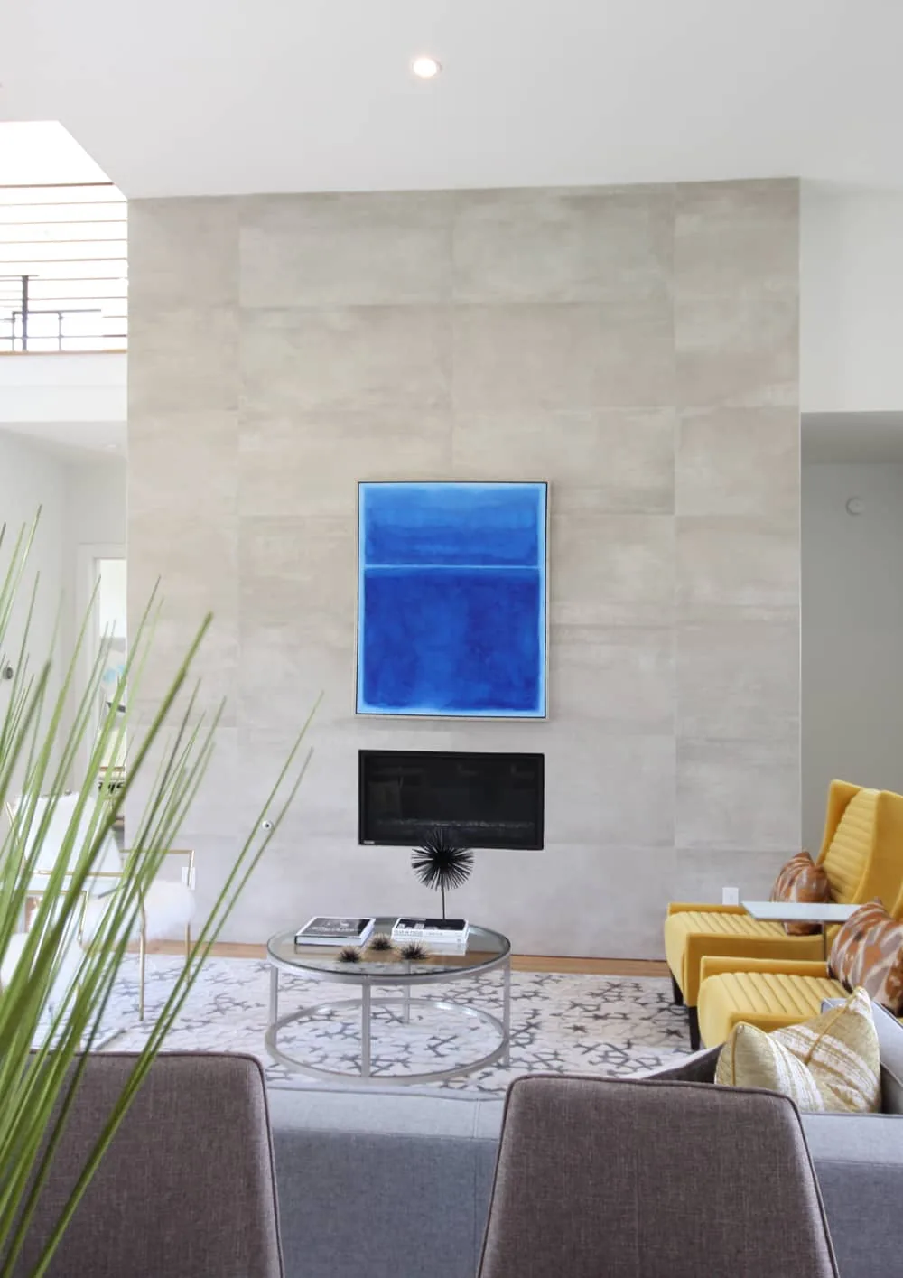 Living room features a light stone tile fireplace wall with a mounted blue abstract painting and yellow upholstered chairs.
