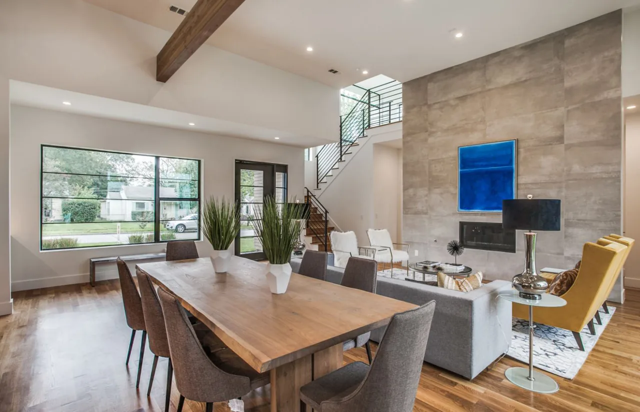 Open two-story living and dining space with concrete fireplace wall and modern furnishings including a gray sofa and yellow armchairs.