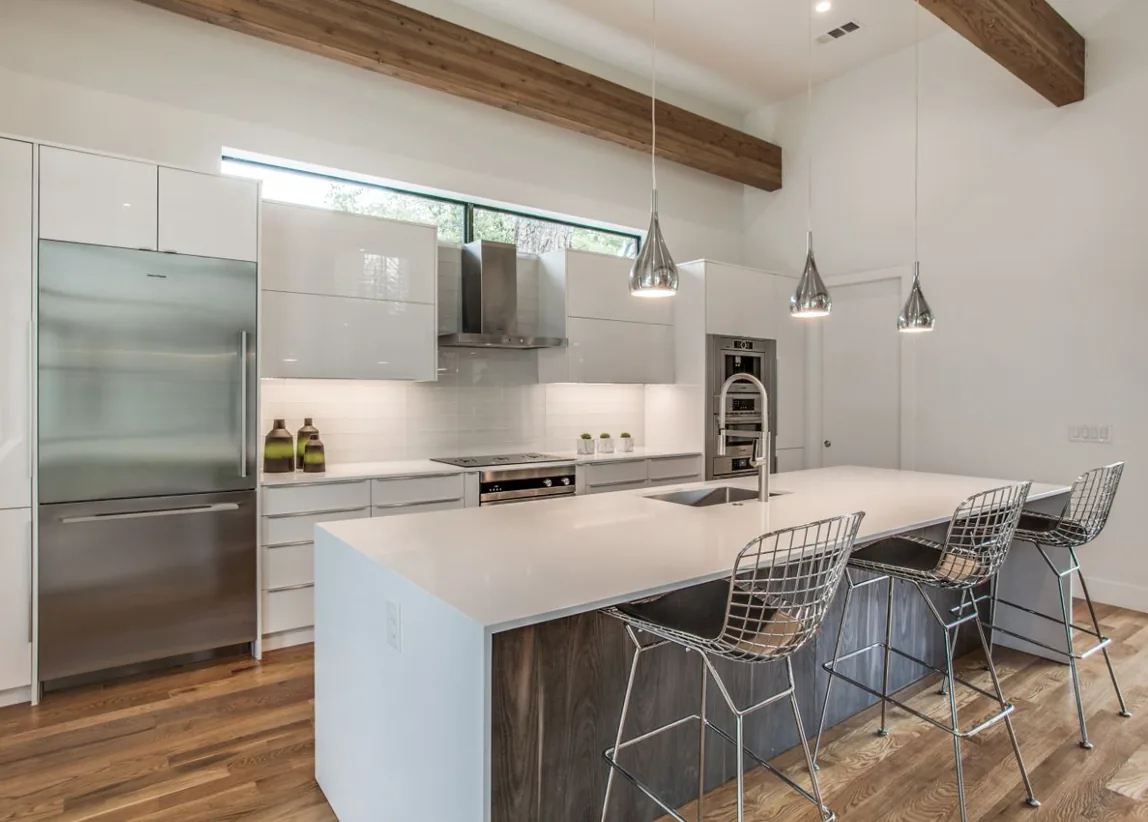 The Ribbon House kitchen features white cabinetry, exposed wooden beams, stainless steel appliances, and a large island with pendant lighting.