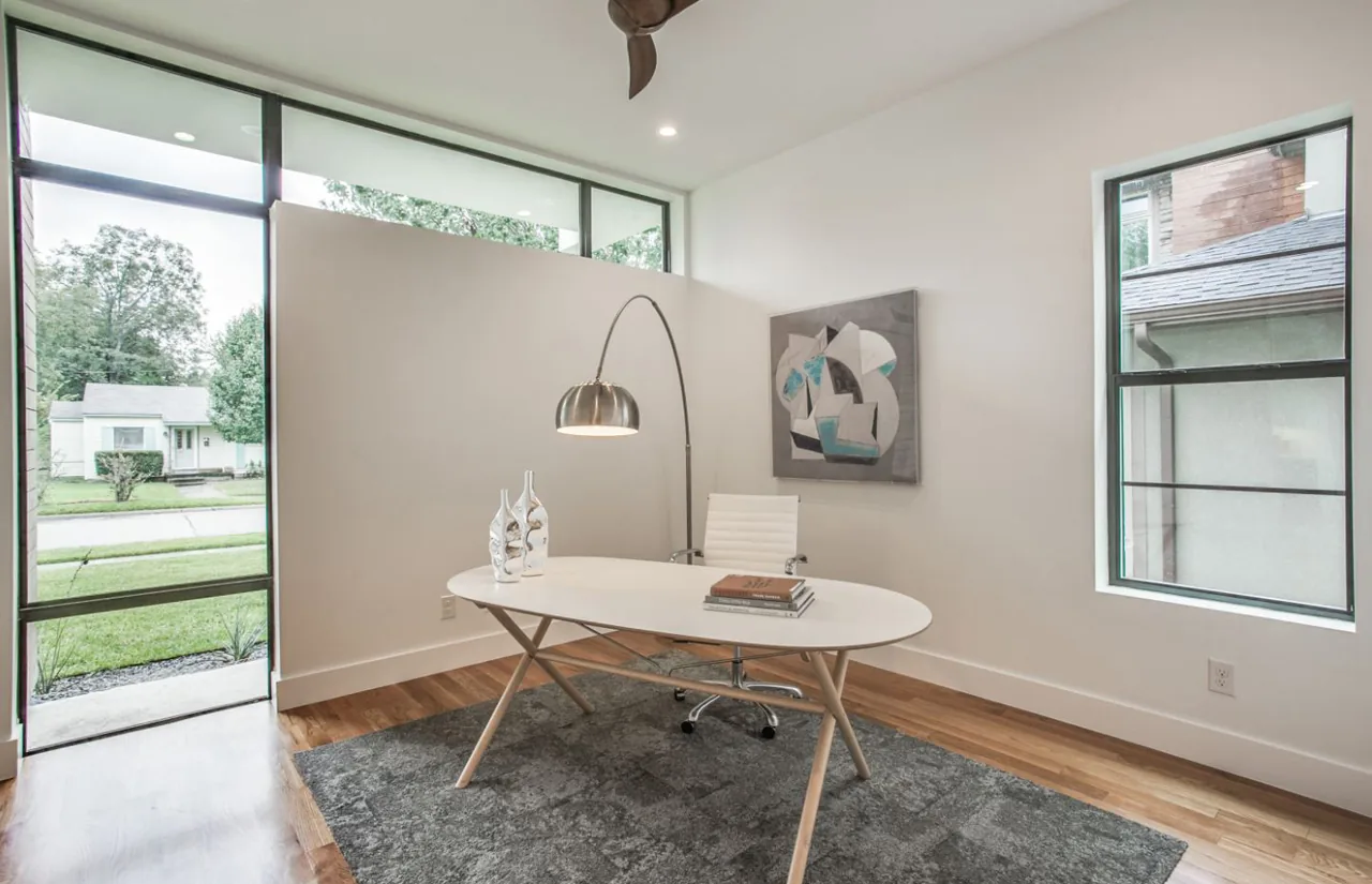 Home office features a white oval desk, arched floor lamp, hardwood floors, and clerestory windows providing daylight.