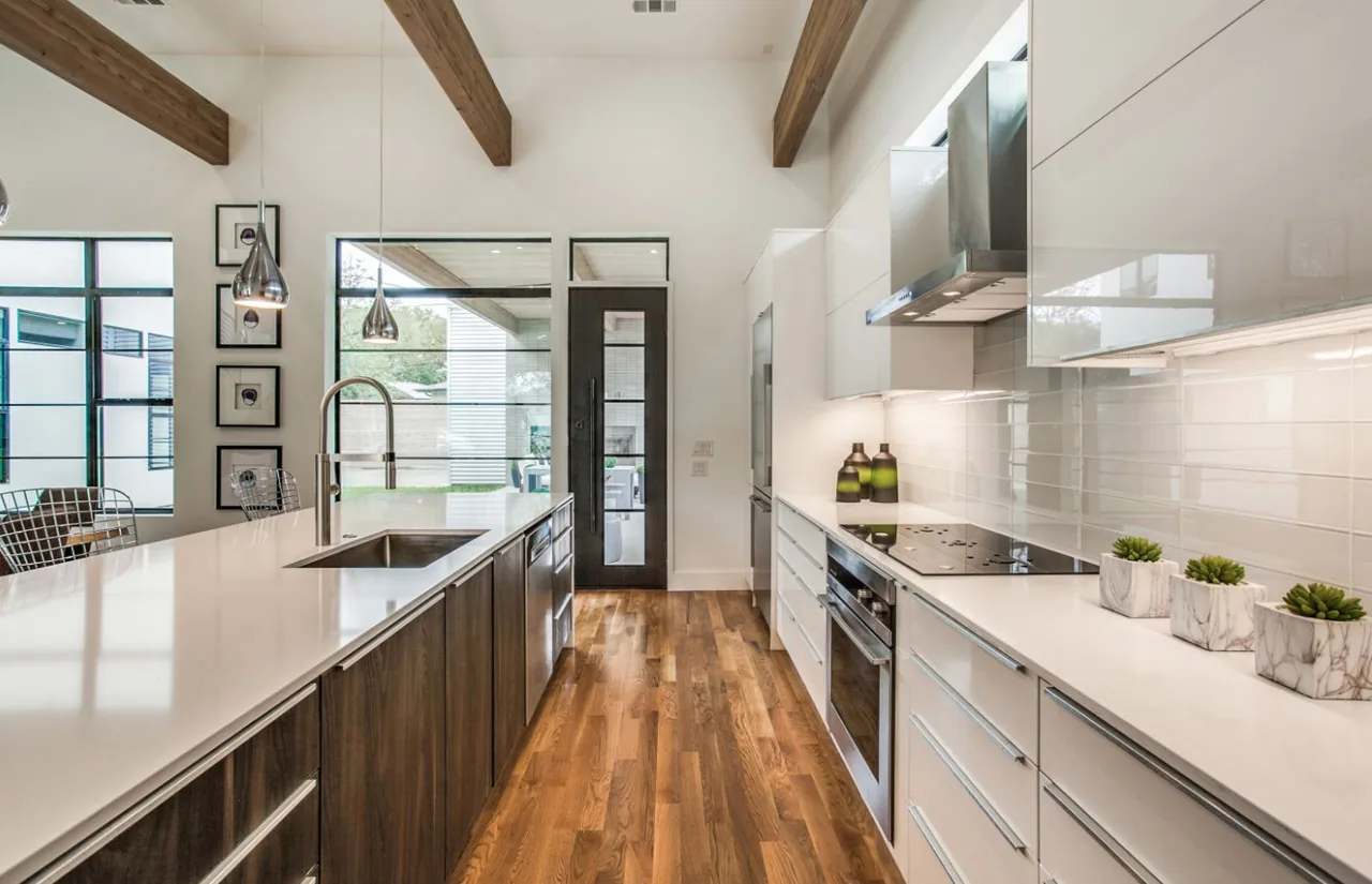 Kitchen in Ribbon House with wood floors, white quartz countertops, and built-in oven under induction cooktop.