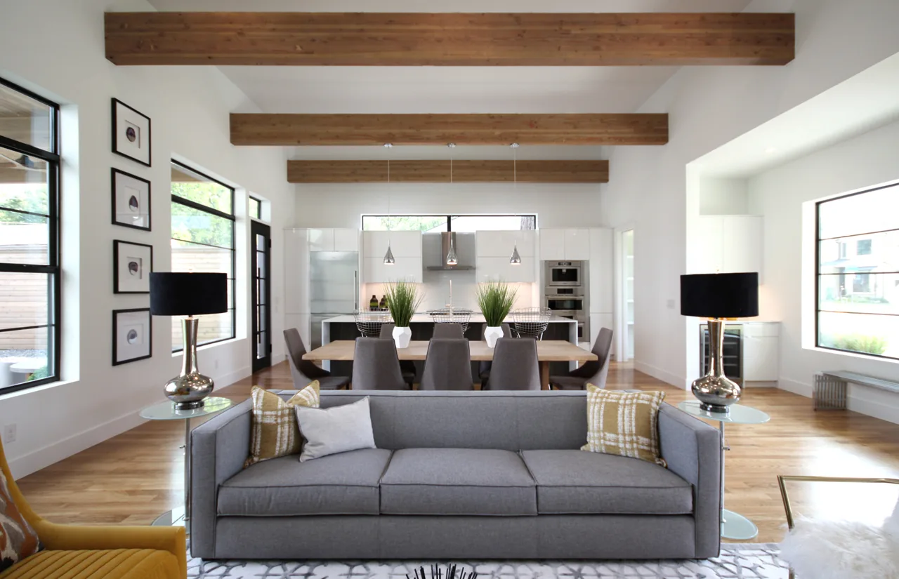 Open layout living and dining room with exposed wood ceiling beams and floor-to-ceiling windows in a modern style.