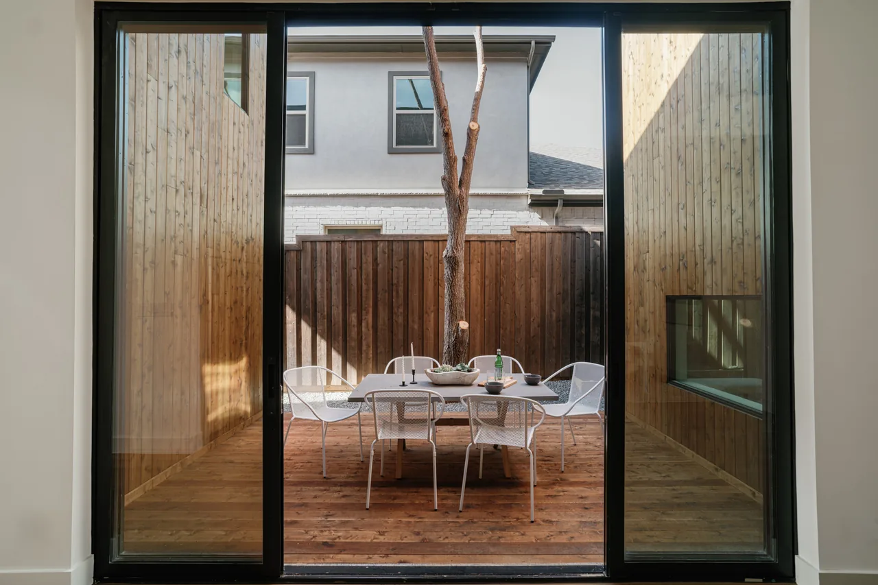 Outdoor dining area with white metal chairs and wood decking in a courtyard fenced with vertical wood panels.