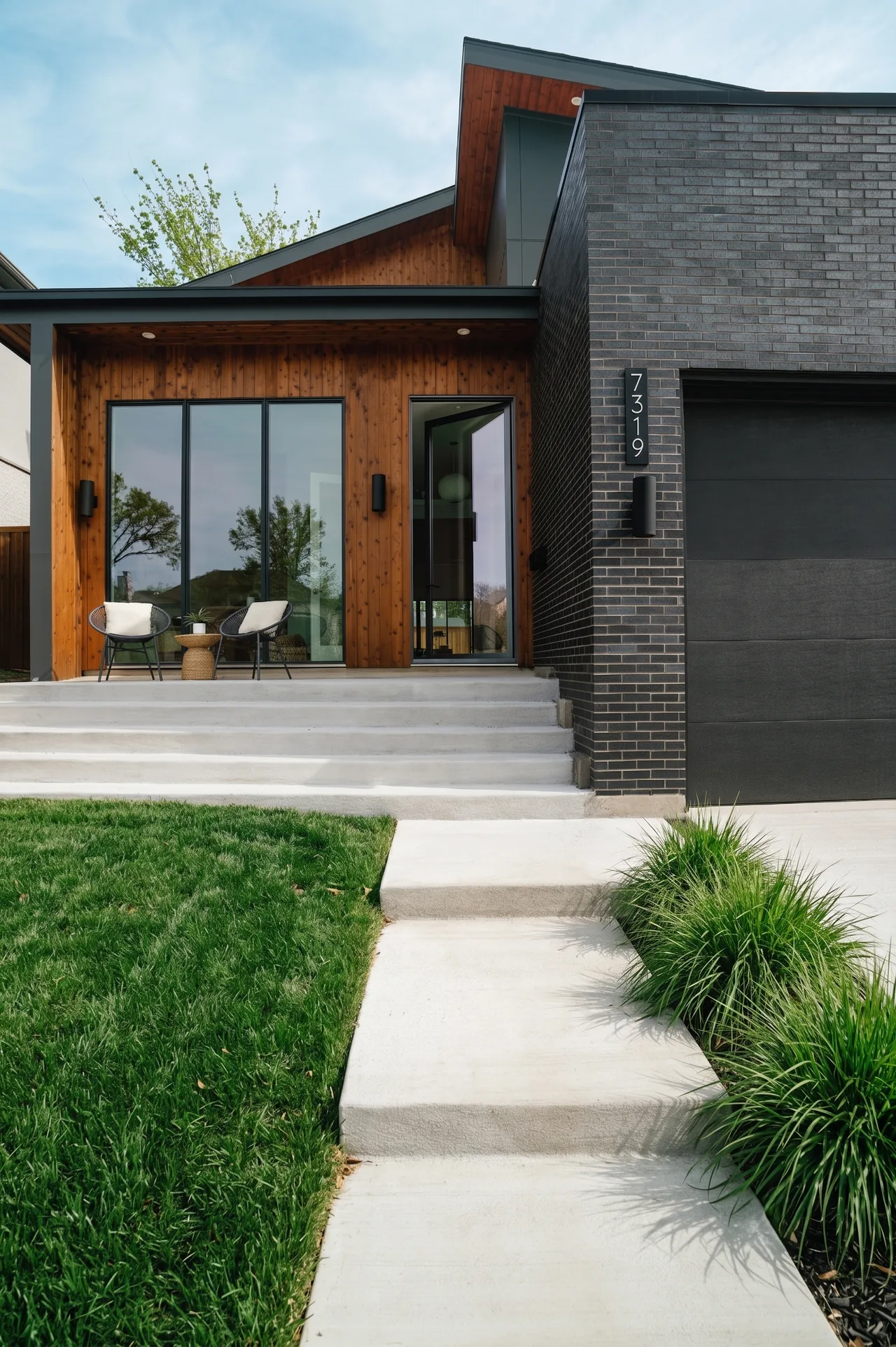 Casa Loma features a modern front exterior with black brick and wood siding accented by concrete steps and an outdoor seating area.