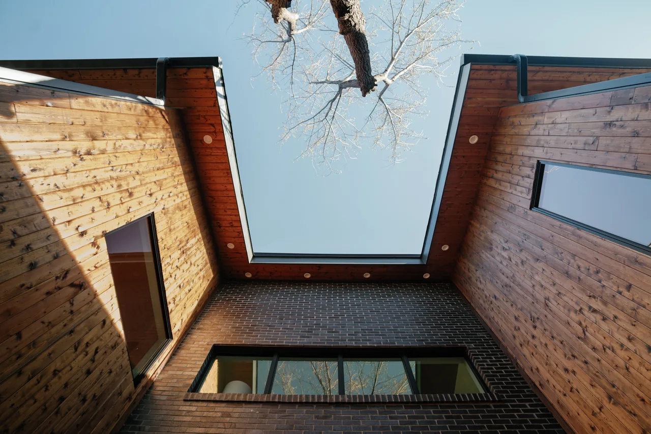 Courtyard view of Casa Loma features wood-sided walls, brick exterior, and black-framed windows under an open sky.