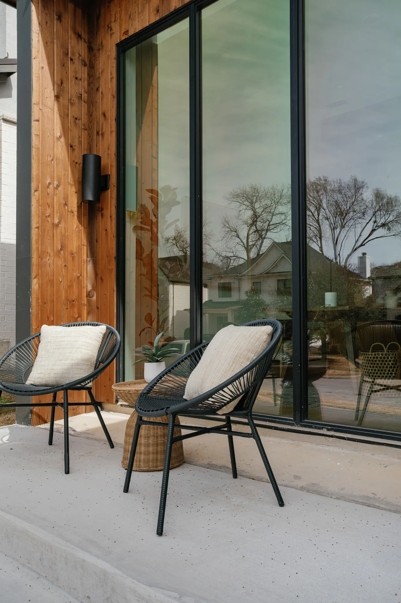 Outdoor seating area on a concrete porch with black window-framed sliding glass doors and wood siding at Casa Loma.