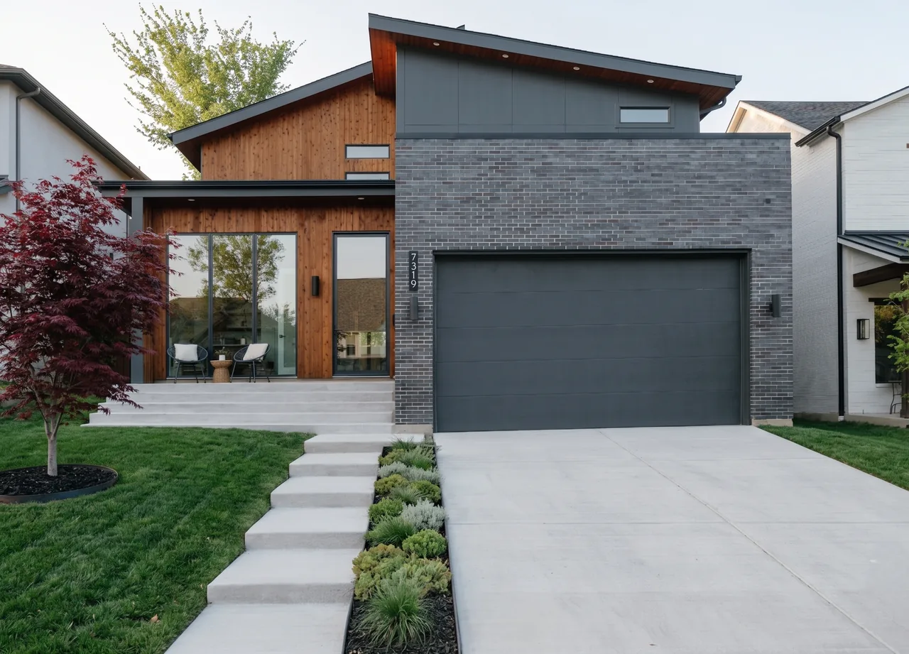 Casa Loma by F+E Architects features a modern exterior with wood siding, dark brick garage, and concrete steps leading to a patio with seating.