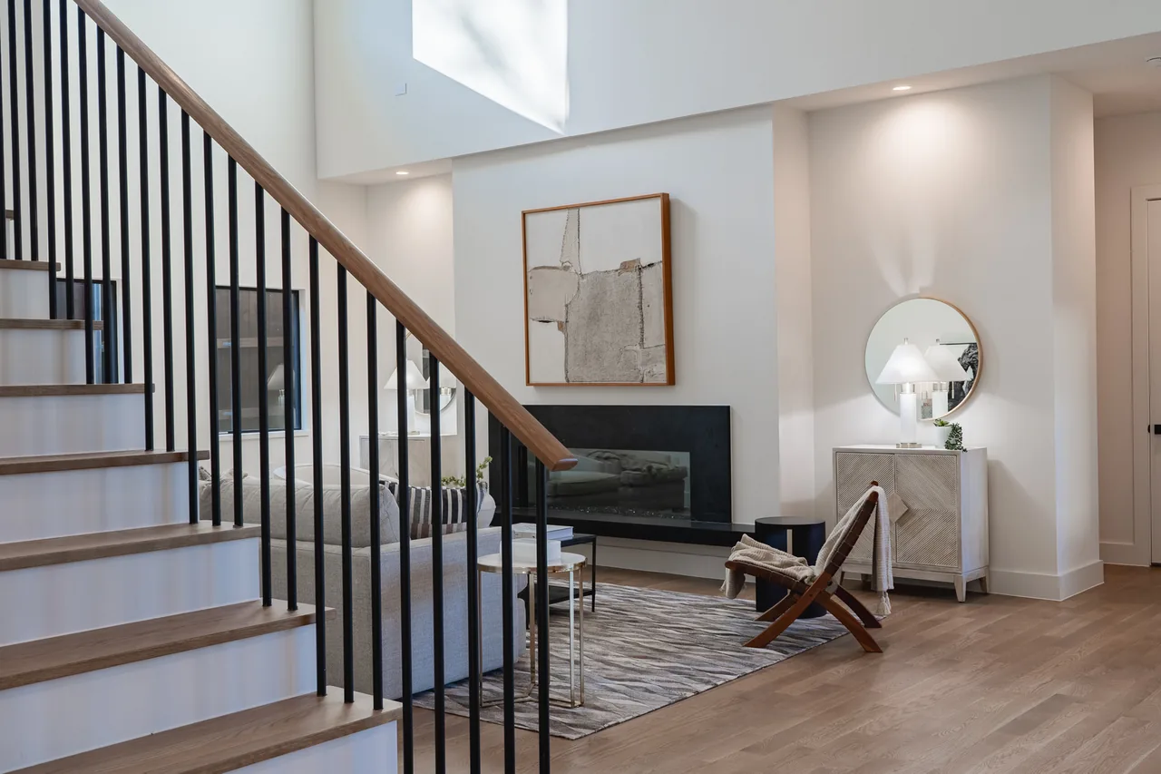 Interior living room with a modern fireplace, staircase with black metal balusters, and natural wood flooring.
