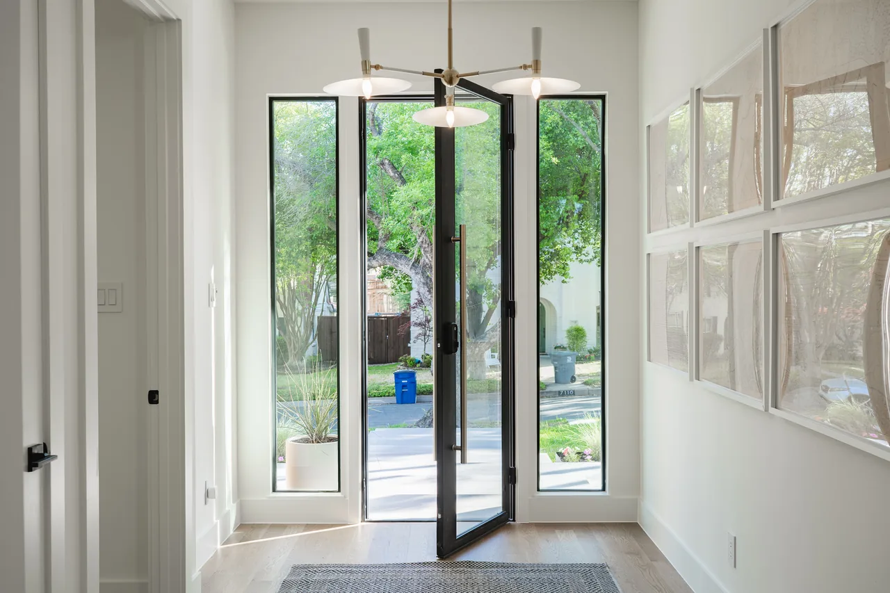 Entryway of Casa Loma II features a black-framed glass pivot door with sidelights and contemporary lighting.