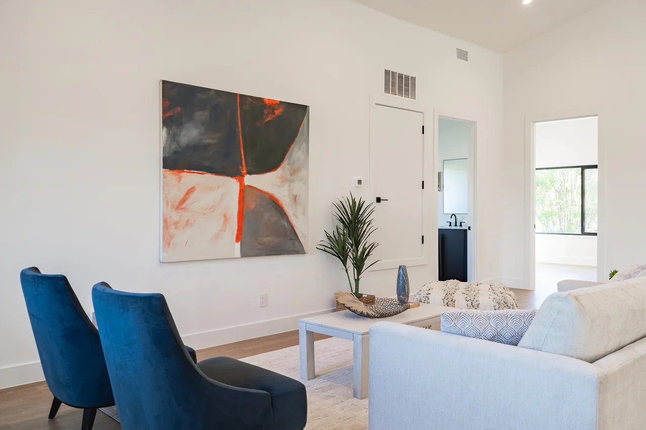Living room featuring blue velvet chairs, a light gray sofa, and an abstract painting by the wall.