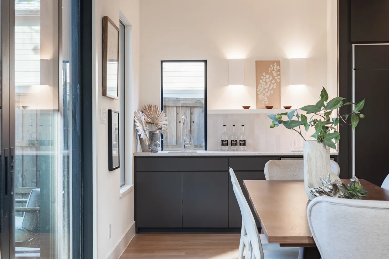 Kitchen with dark lower cabinets, small window, and adjacent dining table with neutral upholstered chairs.