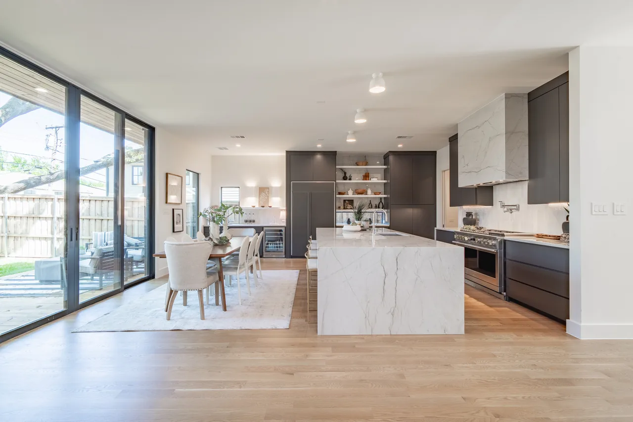 Open floor plan kitchen with marble island, black cabinetry, and light wood flooring.