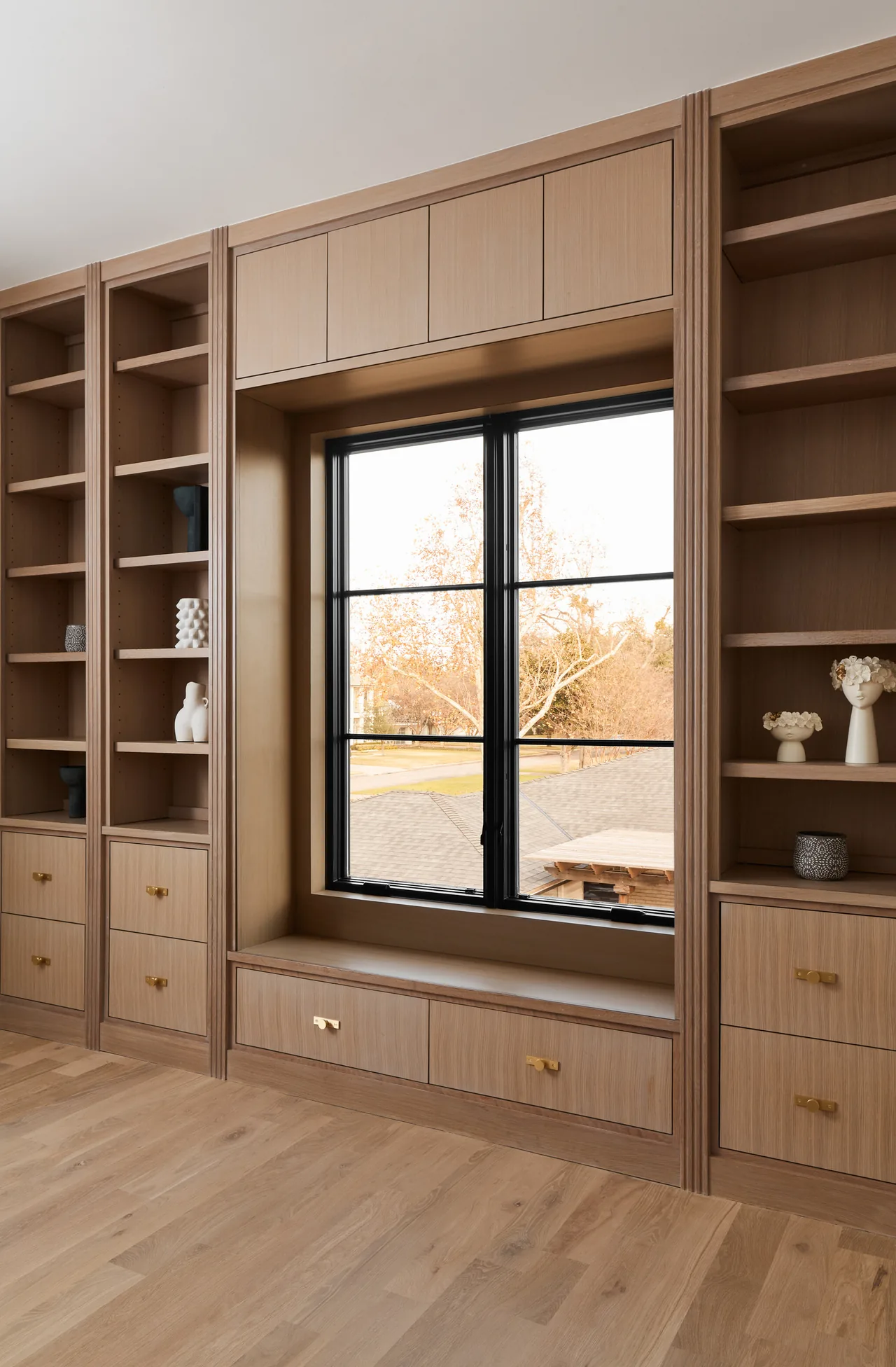 Built-in wood shelves and drawers surround a black-framed window with a window seat below.