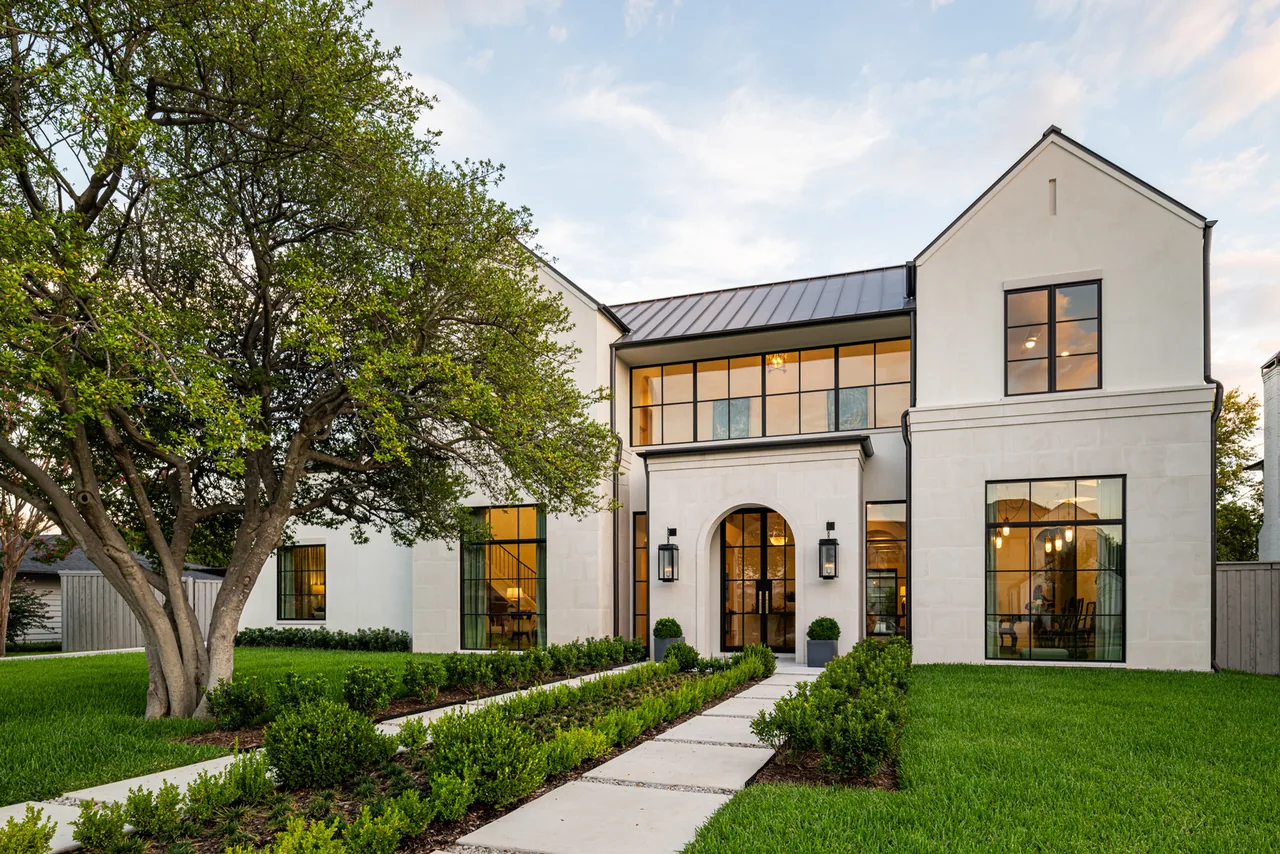Two-story stucco house featuring black window frames and an arched entryway with double glass doors.