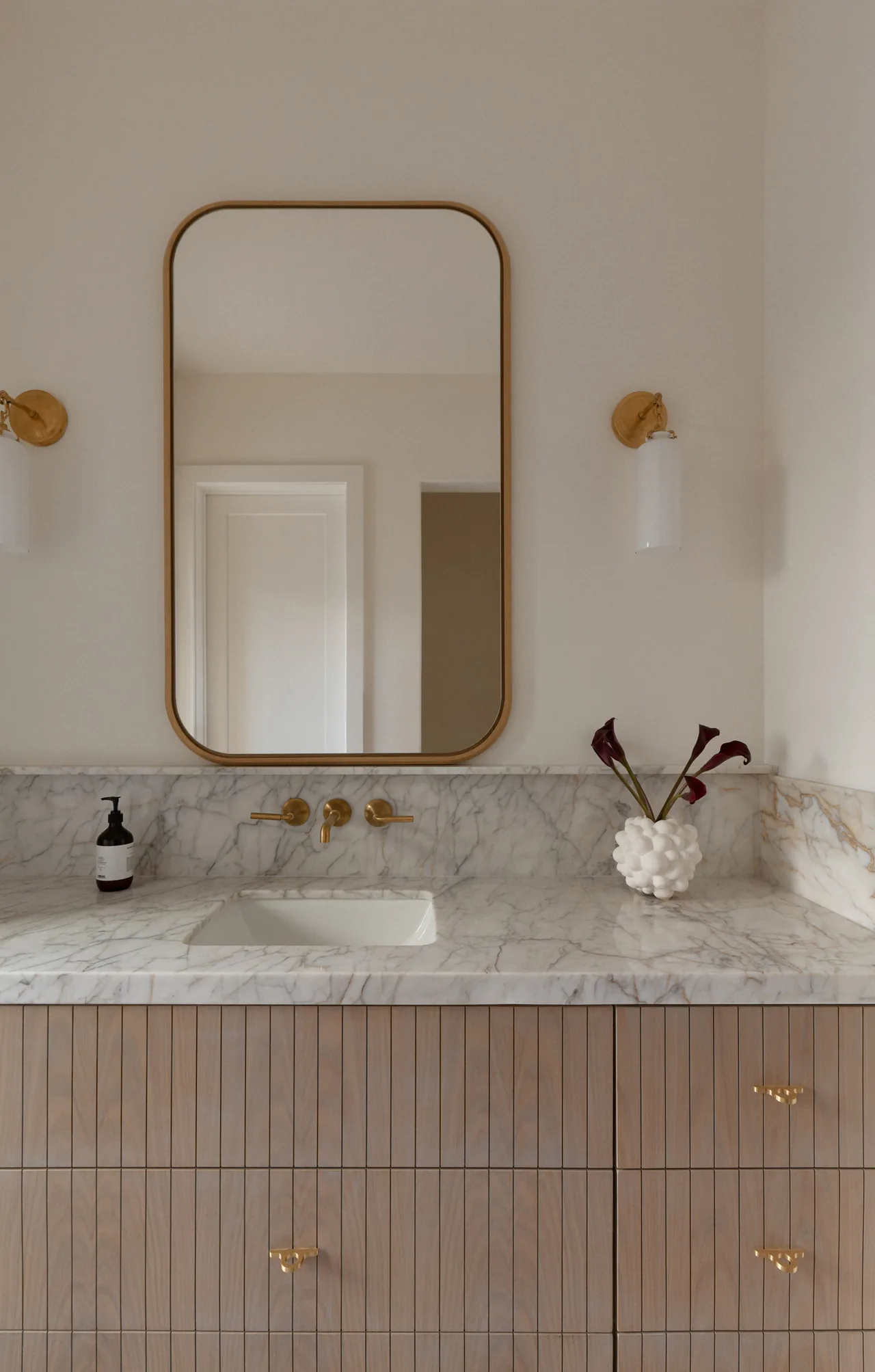 Bathroom vanity features a marble countertop, wood drawers with vertical grooves, and gold wall-mounted faucet and hardware.