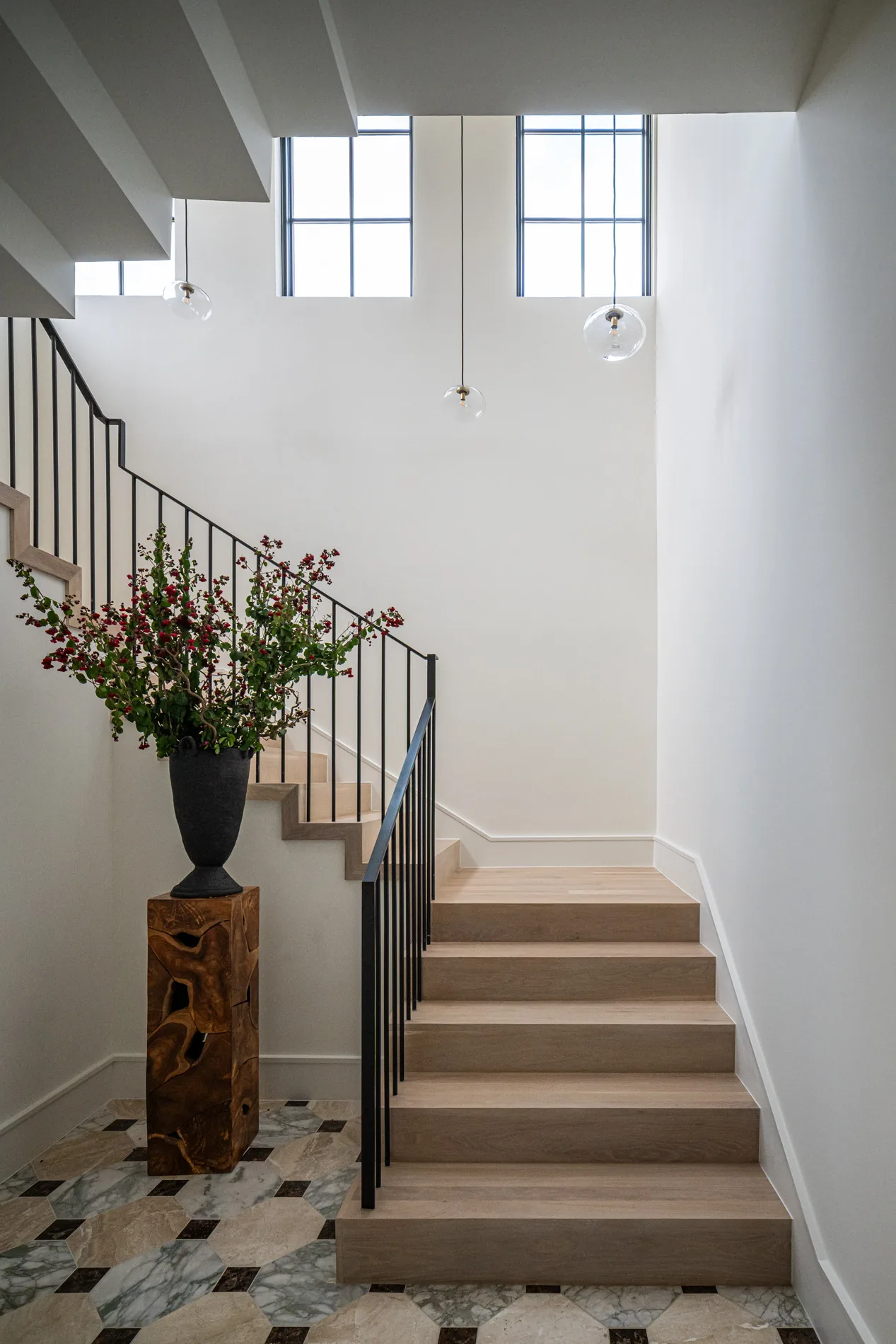 The CABANA LANE staircase features wood steps, black metal railings, patterned tile flooring, and large windows with pendant lights.