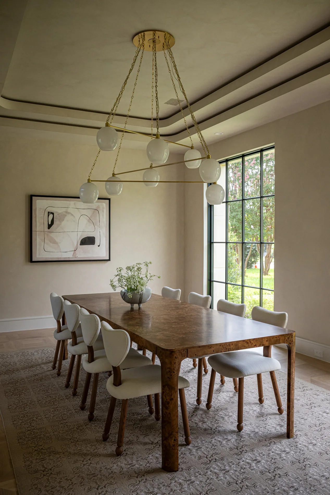 Dining room features a wood-patterned table and a gold chandelier with multiple white globes, next to large grid windows.
