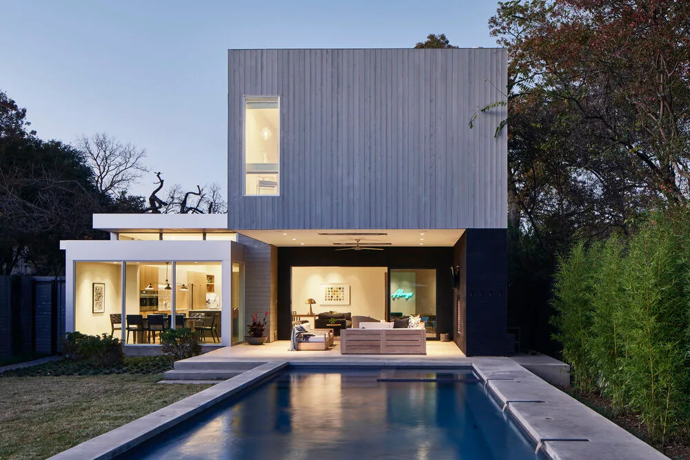 Modern two-story residence with vertical wood siding, tall narrow window, and a rectangular pool in the backyard patio area.