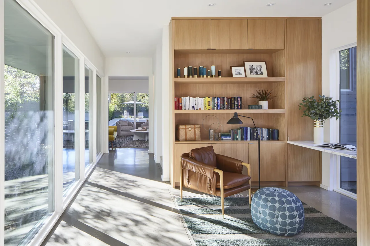Hallway with built-in wood shelving, a leather armchair, and a textured blue pouf at Vanderbilt Residence.