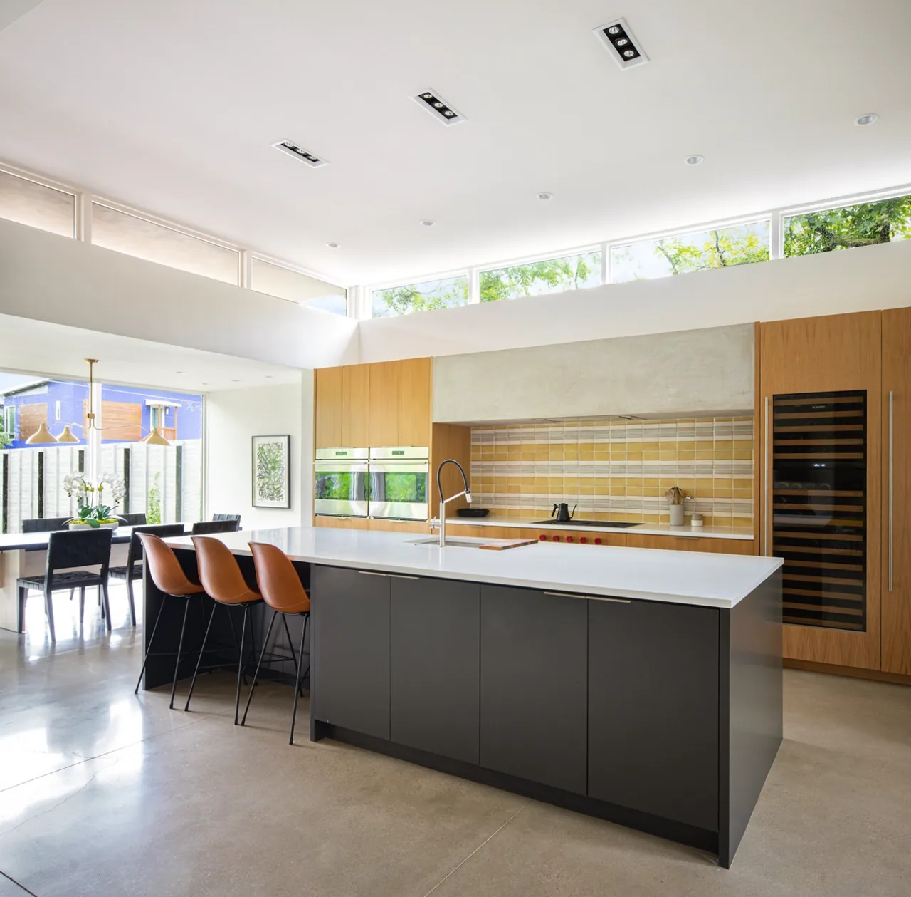 Modern kitchen with a large island, clerestory windows, and tiled backsplash at Vanderbilt Residence in Dallas.