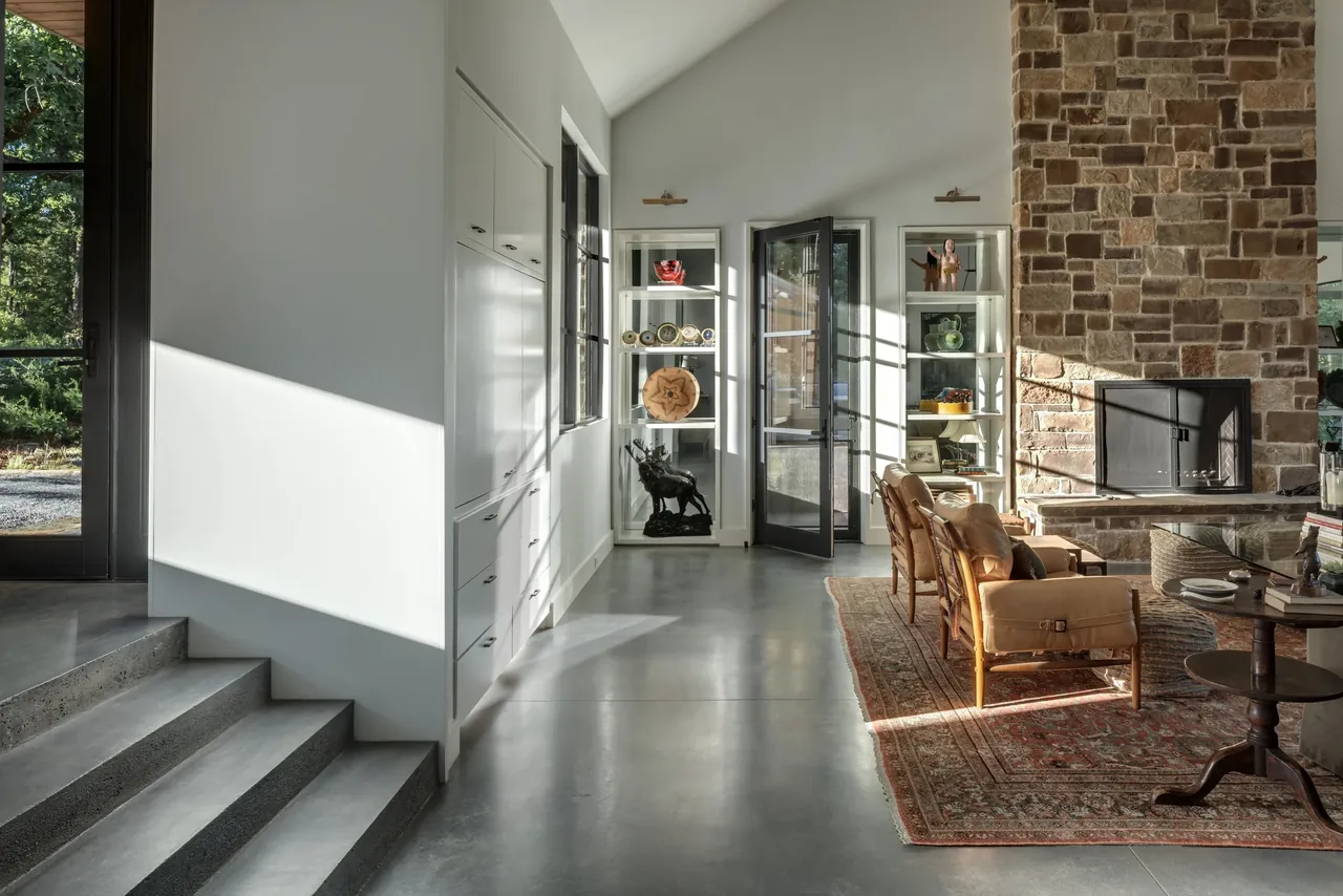 Living room with stone fireplace, concrete steps, and glass door leading outdoors at Pines Ranch project.