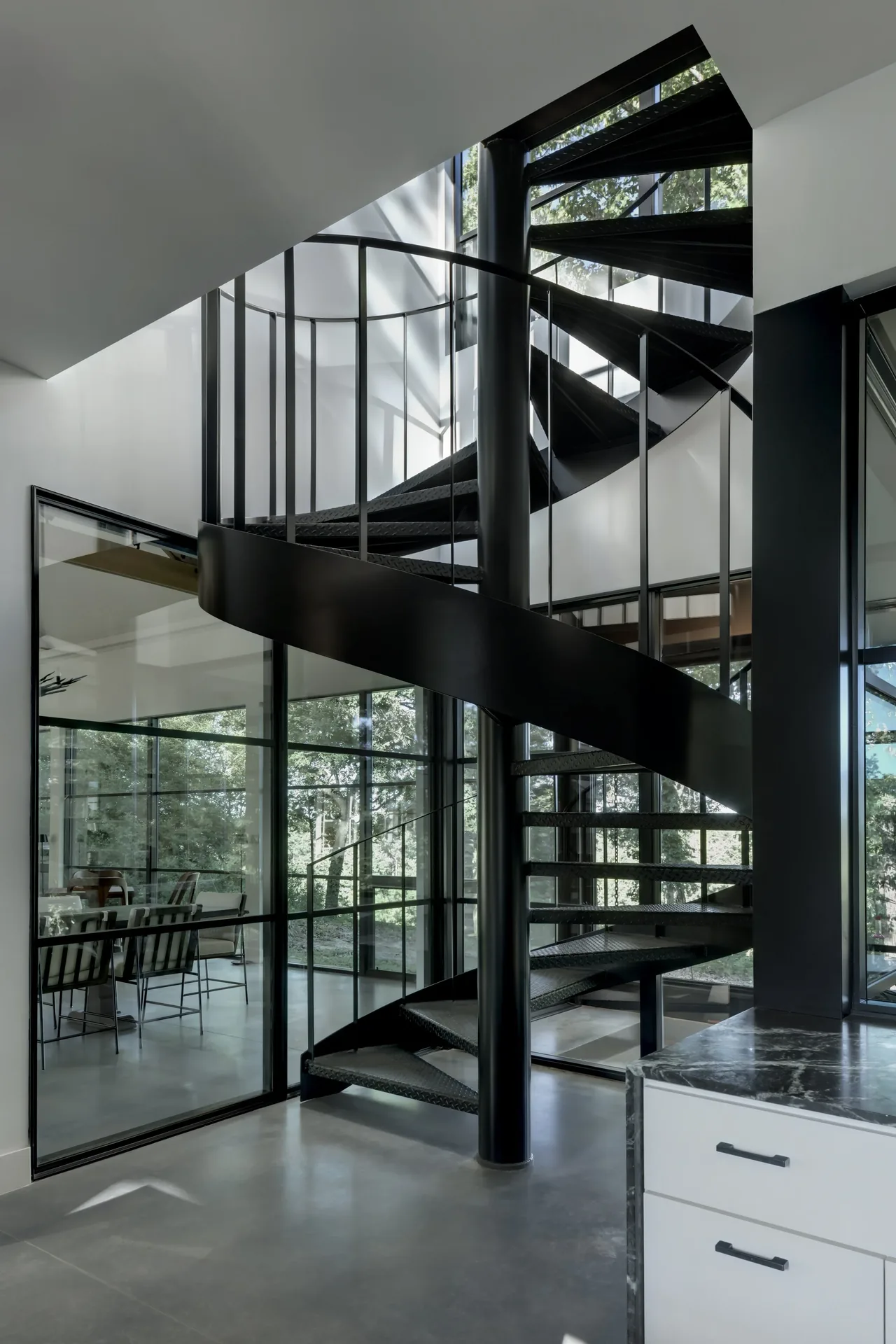 Interior spiral staircase in black metal with large glass windows and concrete floors.