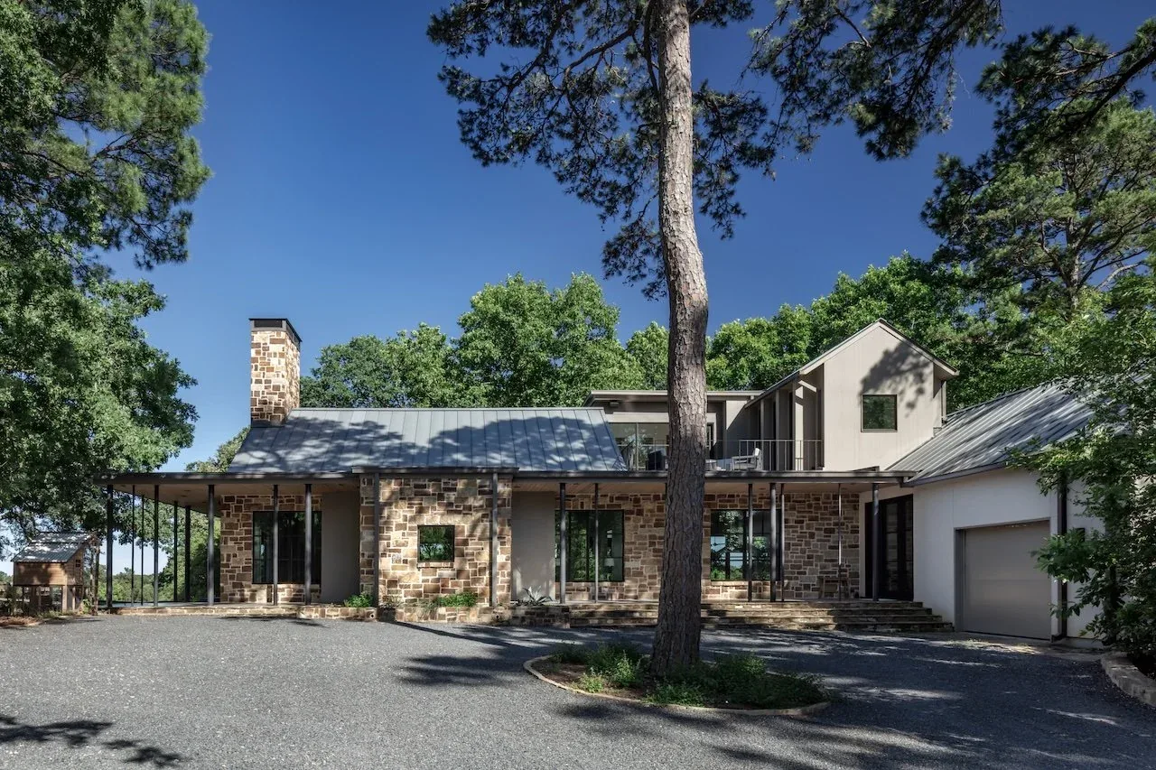 Pines Ranch project by Bentley Tibbs Architect features a stone facade and metal roof under dense pine foliage in Dallas.