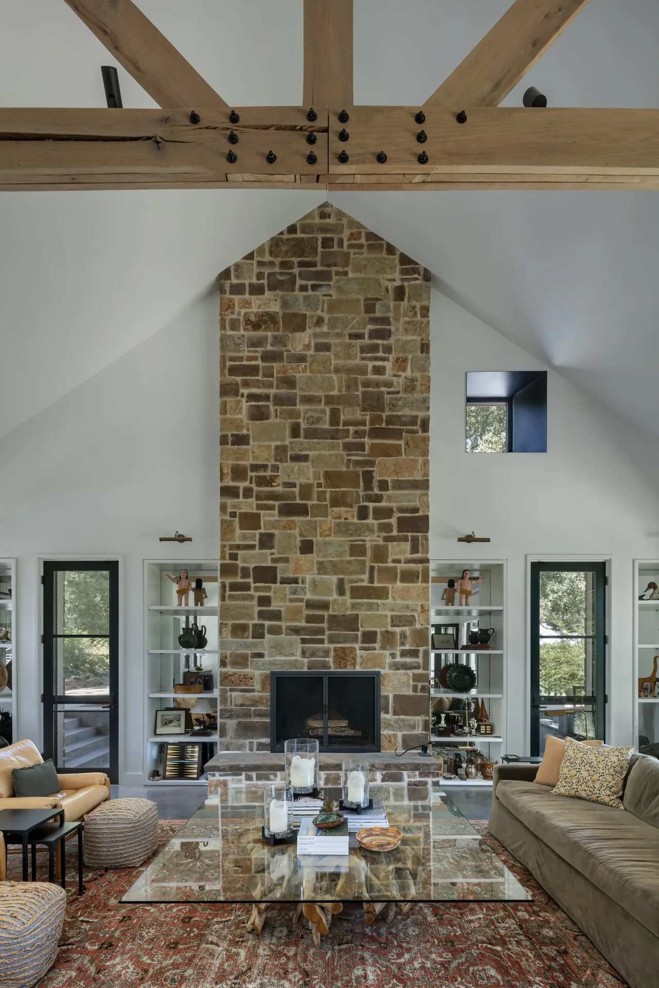 Living room features a vaulted ceiling with exposed wood beams, large stone fireplace, and built-in shelving around doors and windows.