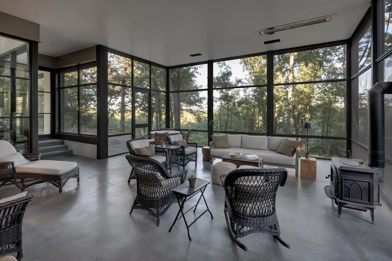Living room with floor-to-ceiling black window frames, concrete flooring, wicker furnishings, and a black wood stove.