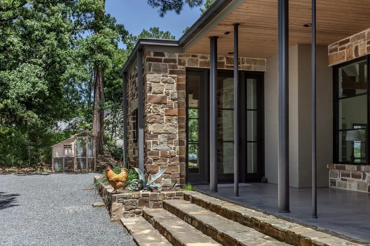 The front exterior of Pines Ranch features stone steps, slender columns, and black window frames under a wood soffit roof.