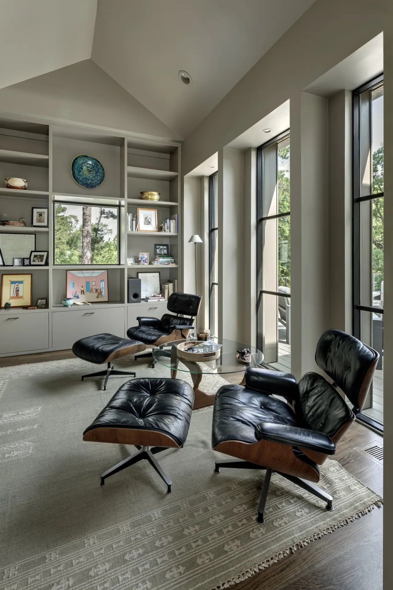 Living room features built-in shelving, vaulted ceiling, and large windows overlooking trees.