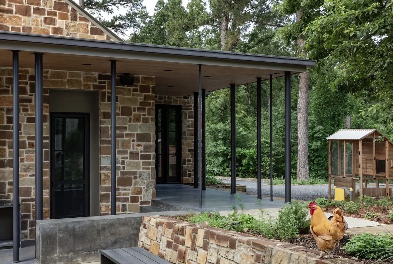 Stone exterior home with a wood soffit ceiling porch, slender black columns, and a small wooden chicken coop.
