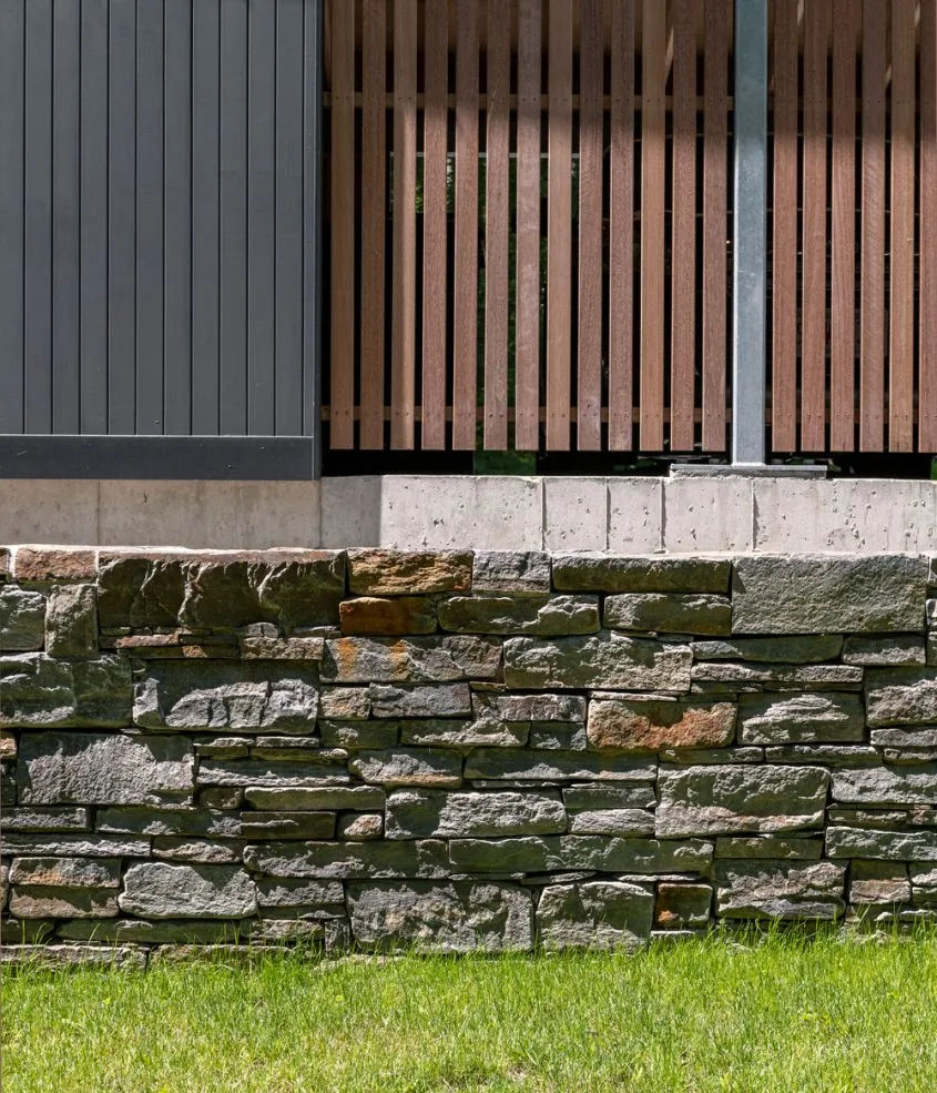 The addition features a stone retaining wall below a concrete base with vertical wooden slats and dark vertical wood siding.