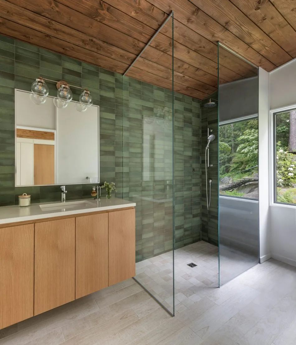 Bathroom features green tile wall, wood ceiling, floating vanity, and open glass shower with natural light from large window.
