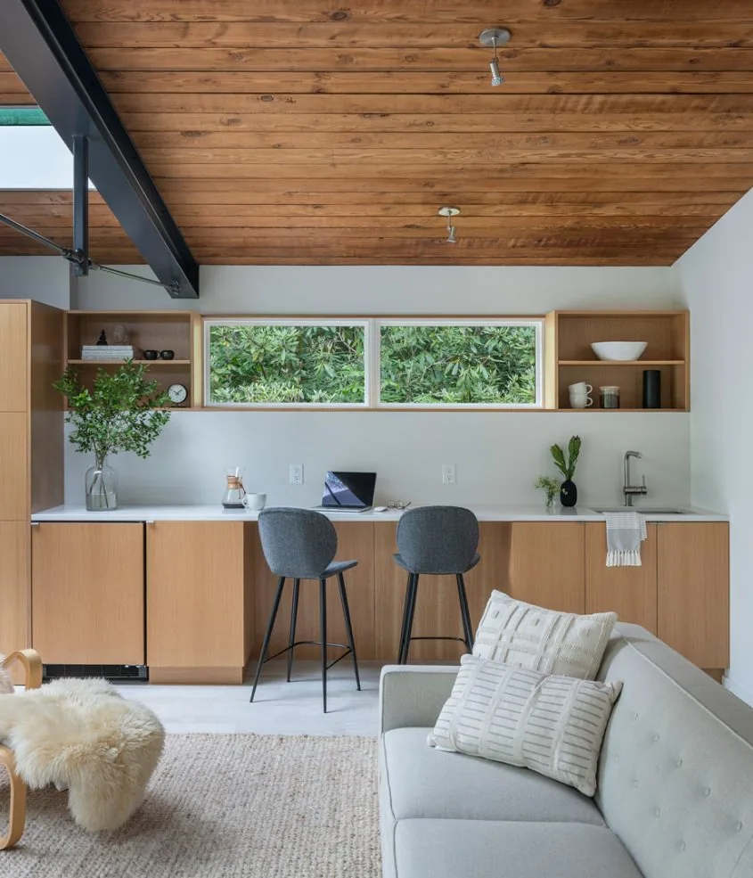 Kitchen with natural wood cabinets, a white countertop, and a horizontal window showing lush greenery.